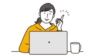 パソコンの前で、左手の人差し指を立てて微笑んでいる女性